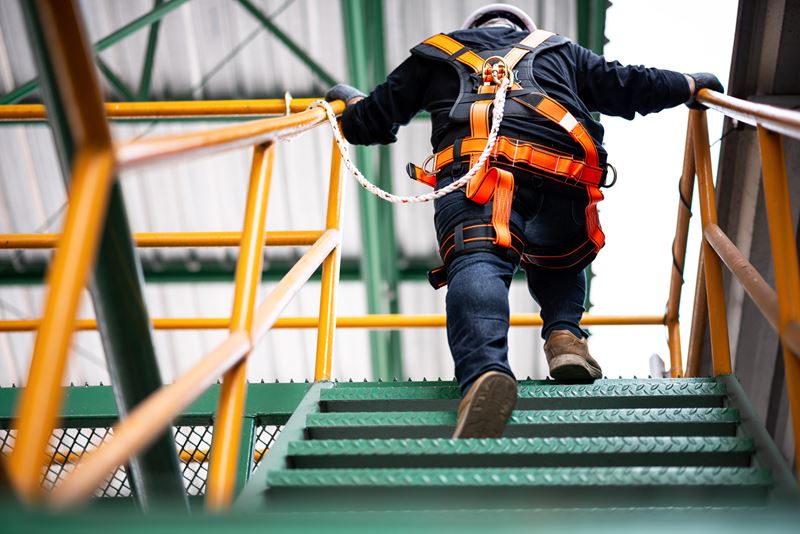 A construction worker is wearing a safety harness and safety line while climbing the stairs.